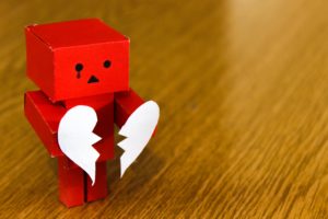 Crying Red Amazon Danbo on Brown Wooden Surface holding brown heart