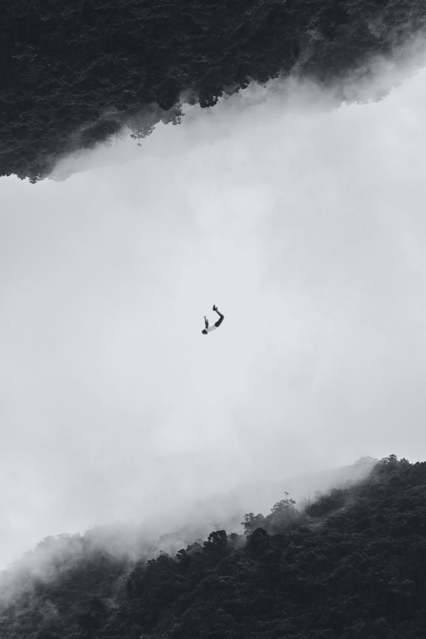 Balck and white picture of person free diving in the sky over foggy forest.